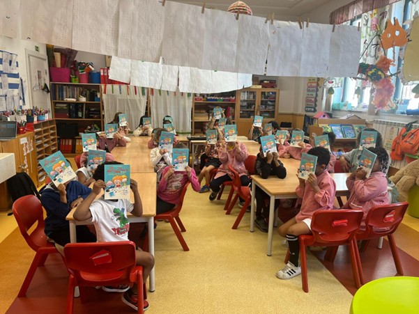 Children in a school room holding copies of the book ZigZaga na Net to cover their faces for privacy.