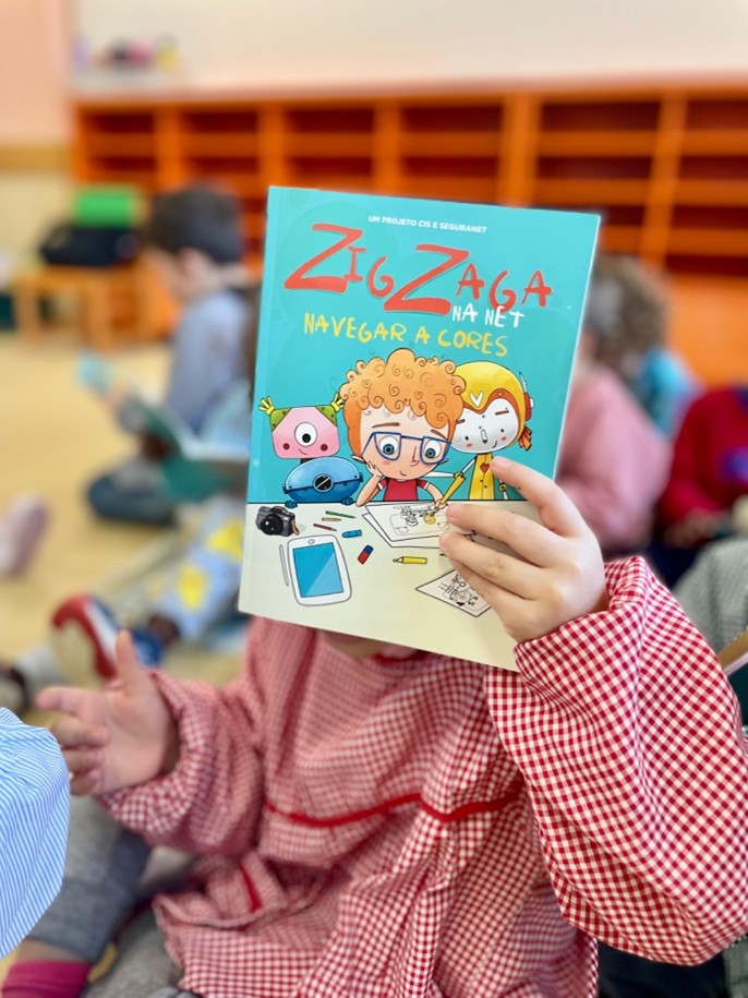 A young pupil covering their face with a copy of the book 'ZigZaga na Net'