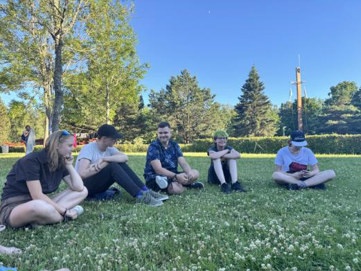 A group of five teenagers discussing while sitting on grass