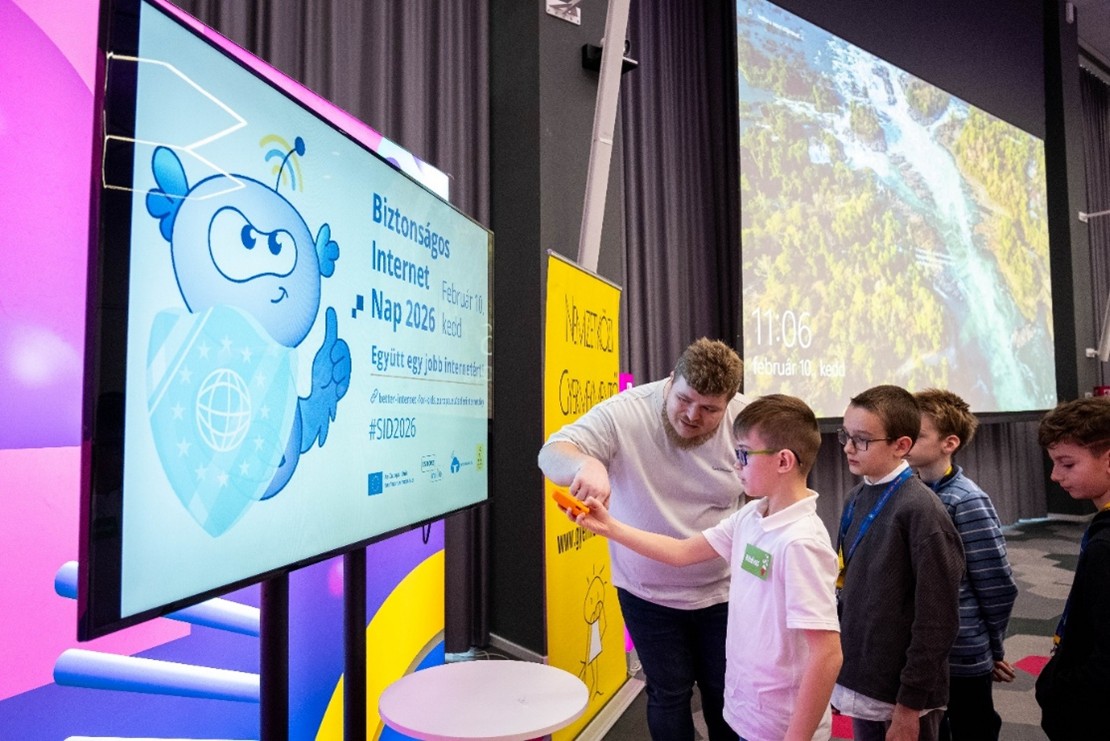 Three children interacting with a screen at the event, helped by a staff member