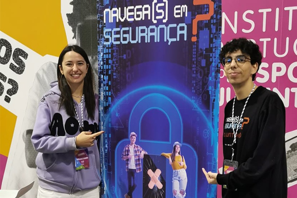 Two young staff members at the fair booth, pointing at a banner on online safety