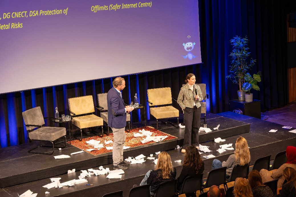 Picthre of the closing panel with Julia van Best and Robbert Hoving on stage. The stage is also covered in paper airplanes previously thrown by the audience members 