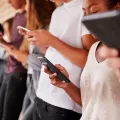 A group of five young people all holding their own smartphone and looking at it.