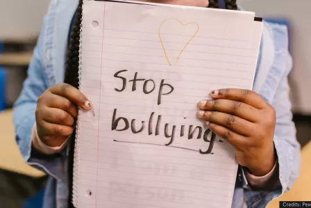 A pair of hands hold a paper sheet upon which is written "no bullying"