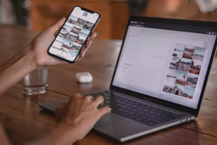 Person at a desk using a mobile phone and laptop simultaneously