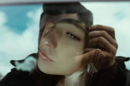 A girl being photographed from inside a car, reflected on the photographer