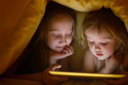 Two young children viewing a tablet under a blanket 'fort'