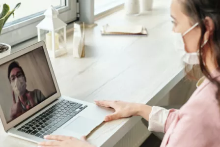 Girl wearing a facemask,seated at a desk using a laptop for online learning
