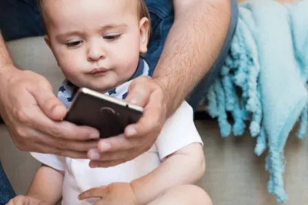 Toddler looking at a phone screen their parent holds for them
