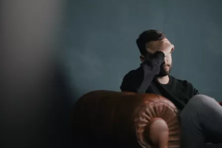 Man sat on a sofa, looking distraught with his head in his hand