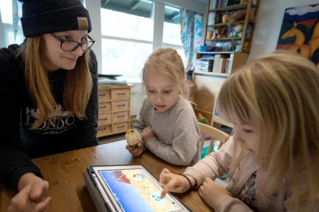 Woman looking over a pair of young girls using a tablet