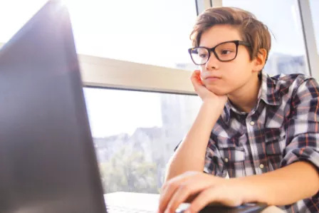 Young boy looking bored using a laptop computer