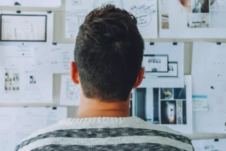 Back view of a man looking at a notice board with lots of posts on it