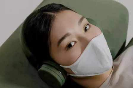 Young woman wearing a mask and listening to something through earphones