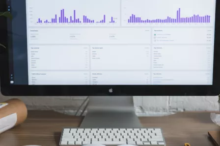 A report showing on a desktop computer screen, and an open notepad on a desk
