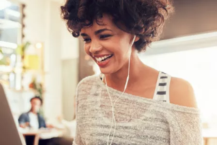 Smiling woman using a laptop, with earphones in