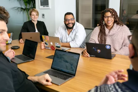 Group of people discussing cheerfully around a table with laptop