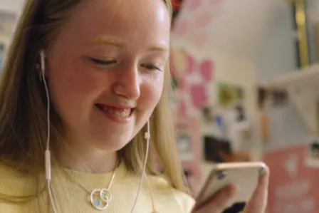Teenage girl smiling while looking down at her smartphone