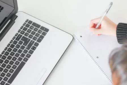Person writing next to a computer