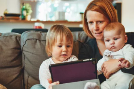 Woman and two children sitting on a couch while looking at a tablet