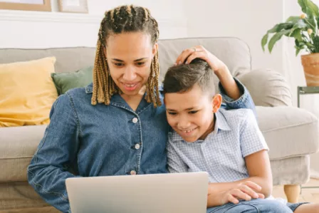 A mother and her son sitting on the floor and looking at a laptop