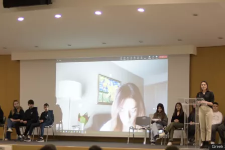People on stage with a screen showing a woman in the background