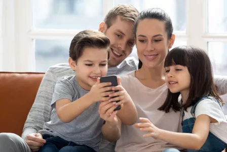 A family of four (mum, dad, boy, girl) all looking at a smartphone sitting on the sofa
