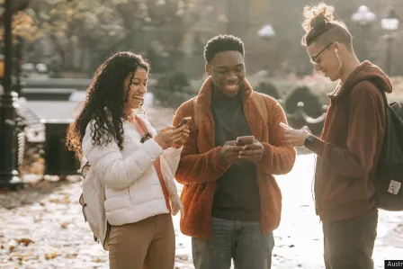 A group of three young people smiling while looking at their smartphones