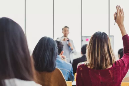 Adults in a seminar setting, with one raising their hand