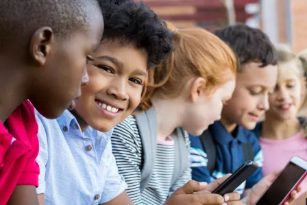 A group of five children looking at smartphones while sitting next to each other