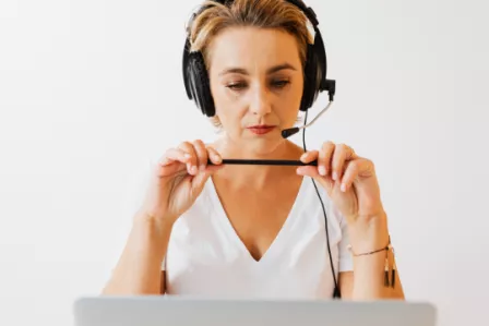 Middle-aged woman wearing a headset, holding a pen and looking at her computer screen