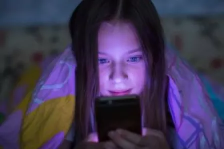 young girl in the dark holding a phone with blue light
