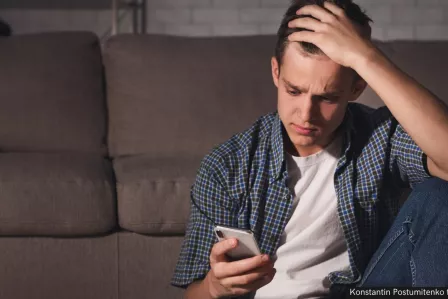 A young man stares at his phone screen in distress