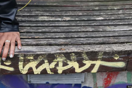 The detail of a hand and hips of a person sitting on a wooden bench.