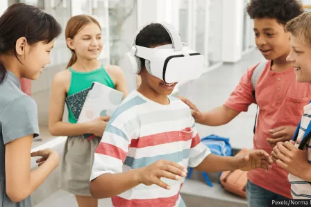 A group of five children in a circle, one of them is wearing a white headset.