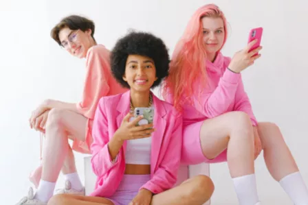 Three diverse teenagers dressed in pink holding smartphones and smiling at the camera