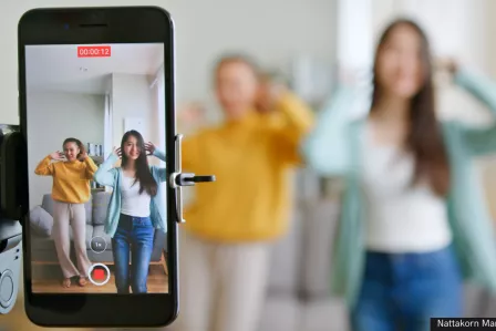 Two adolescents dancing in front of a smartphone on a tripod, recording themselves.