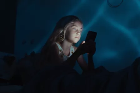 Little girl looking at a smartphone with blue light in the background