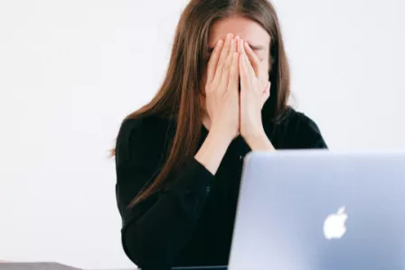 Girl covering her face in dismay in front of a laptop sreen