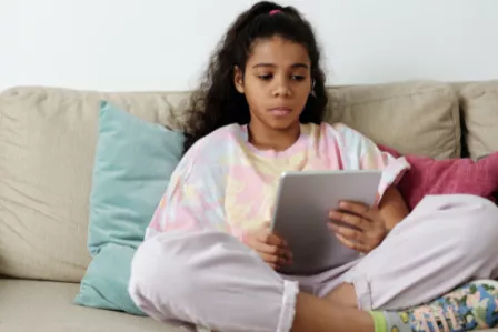 Child sat on a sofa reading on a tablet device