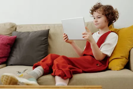 A girl sitting on a sofa and holding a white tablet