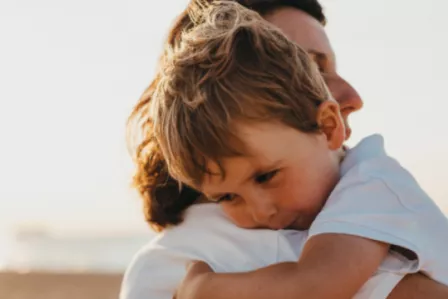 A sad young child being held by a parent or carer