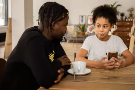 A parent talking to his daughter holding a phone
