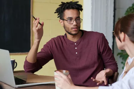 A man holding a pen discussing with a woman in front of a laptop