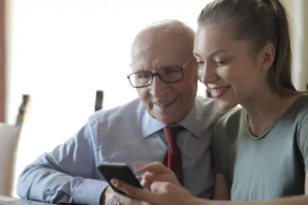 Elderly person looking at smartphone together with younger woman