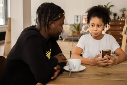 A dad talking to his concerned daughter holding a smartphone