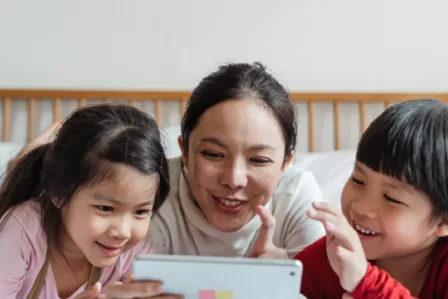 A mother and her two children playing on a tablet and laughing