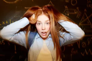 A teenage-girl with long red hair pulling out her hair in distress.