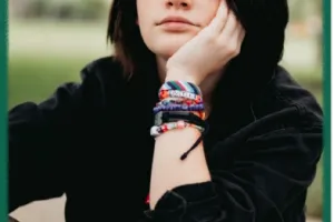 Girl with black hair looks into camera, sitting outside in a park.