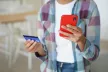 A young person holding a red smartphone in one hand, and a credit card in the other hand